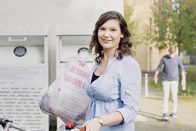 Kleidersammlung des DRK und Altkleidercontainer: junge Frau mit Altkleidersack vor einem Container des DRK- 2014